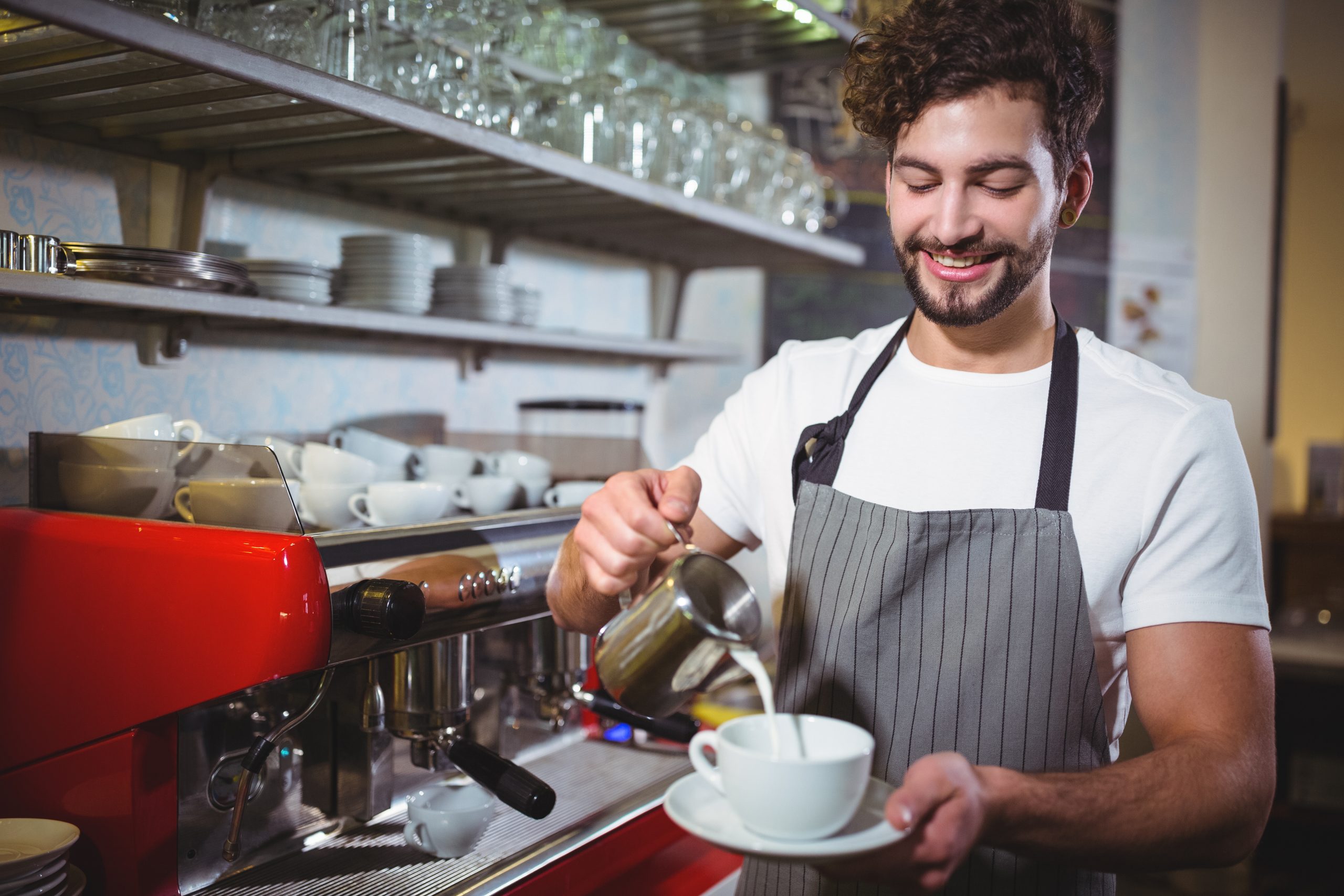 Smiling waiter making cup of coffee at counter in cafe